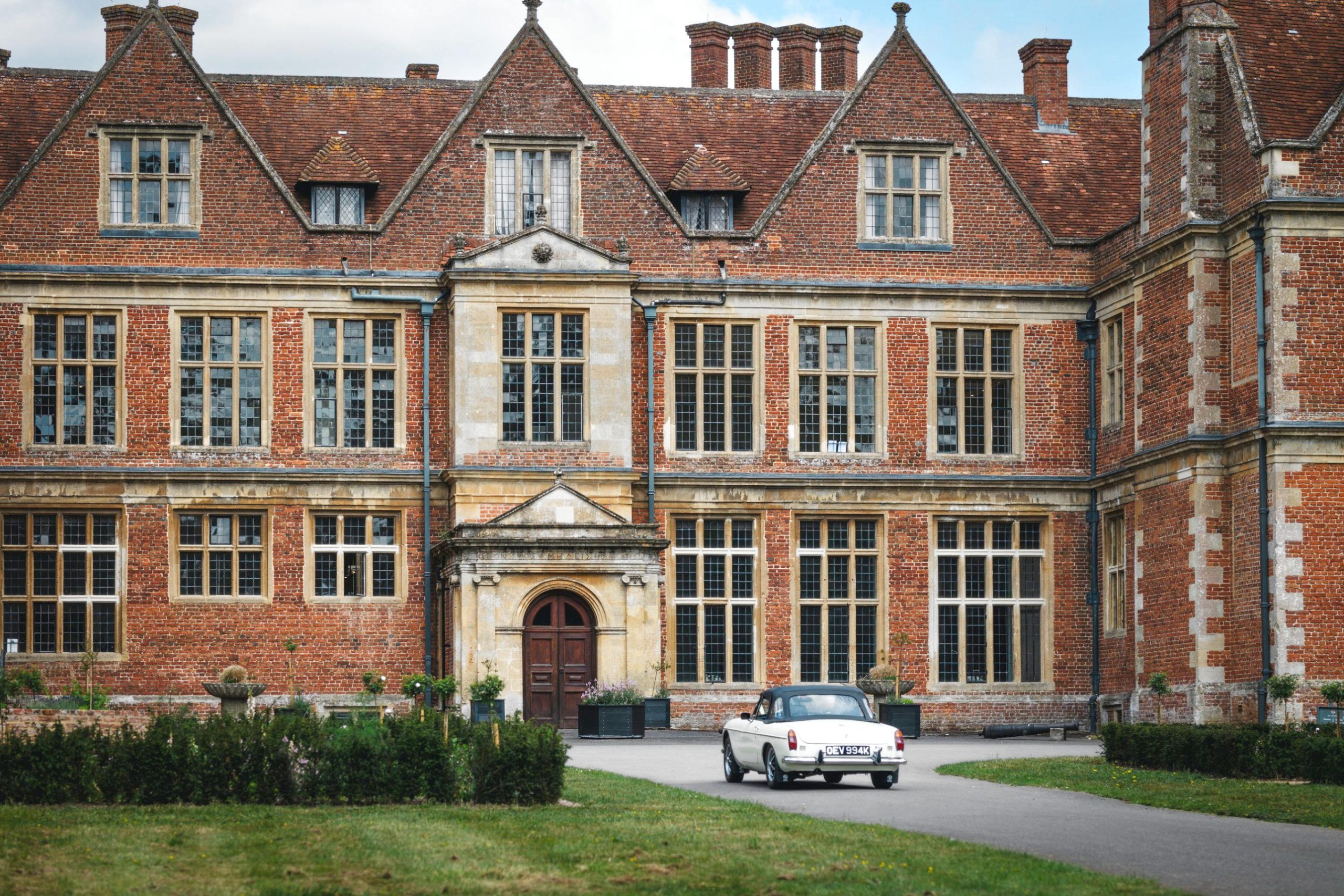 A classic white sports car pulls up to the red-brick front of Shaw House, Newbury