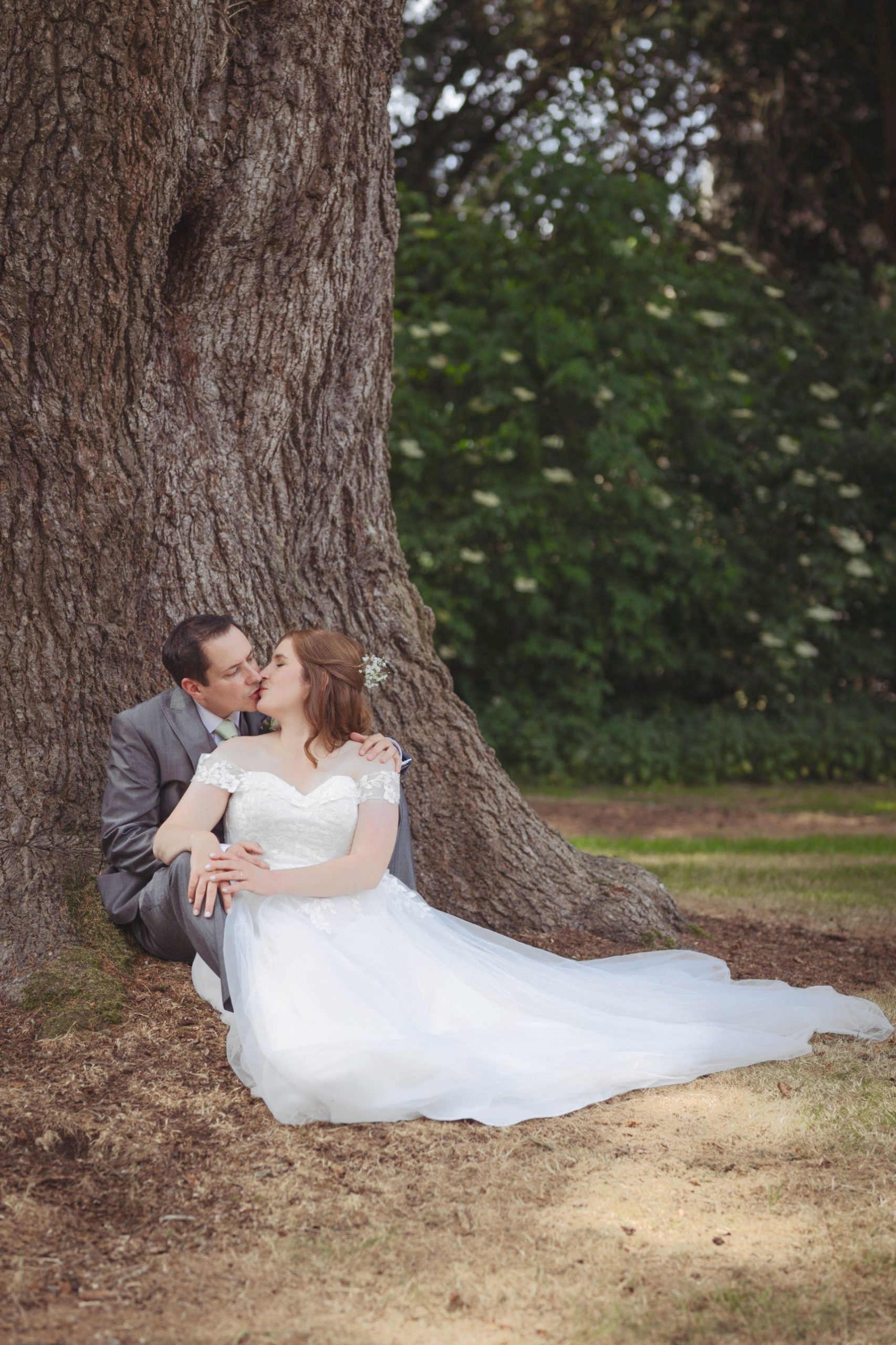 A bride and groom kiss beneath a tree in the grounds of Shaw House